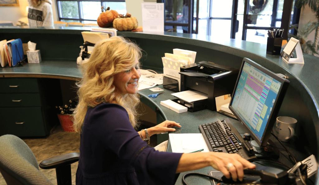 A blonde receptionist wearing a purple shirt about to answer the phone with a smile on.
