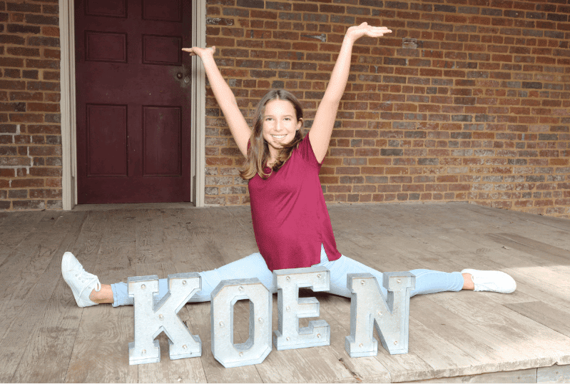 Adolescent girl doing a split in front of Koen sign