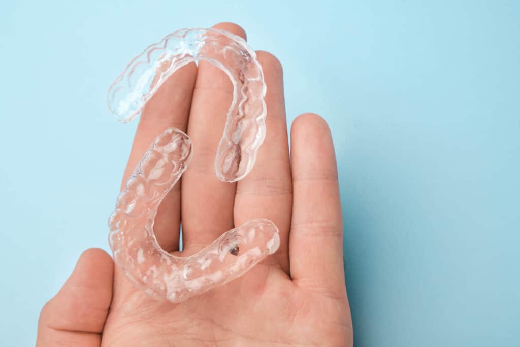 two invisalign aligners on the palm of a patient's hand in front of a blue background