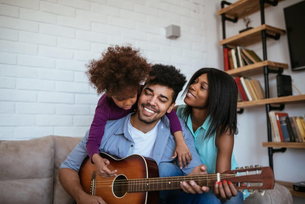 a dad playing the guitar while his daughter and wife sit next to him