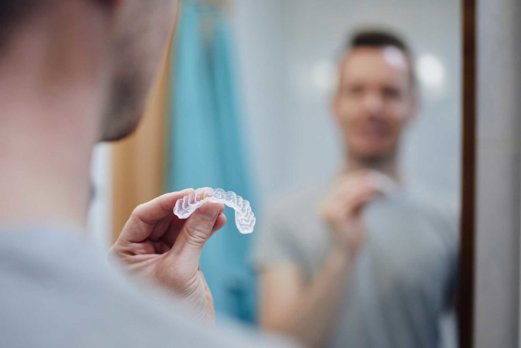 a man holding his invisalign clear aligners in front of his bathroom mirror