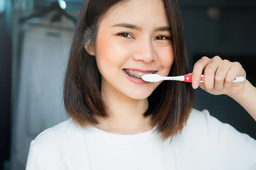 a young woman with braces brushing her teeth with a regular toothbrush