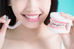 a woman holding up invisalign aligners in one hand and a typodont model on the other hand