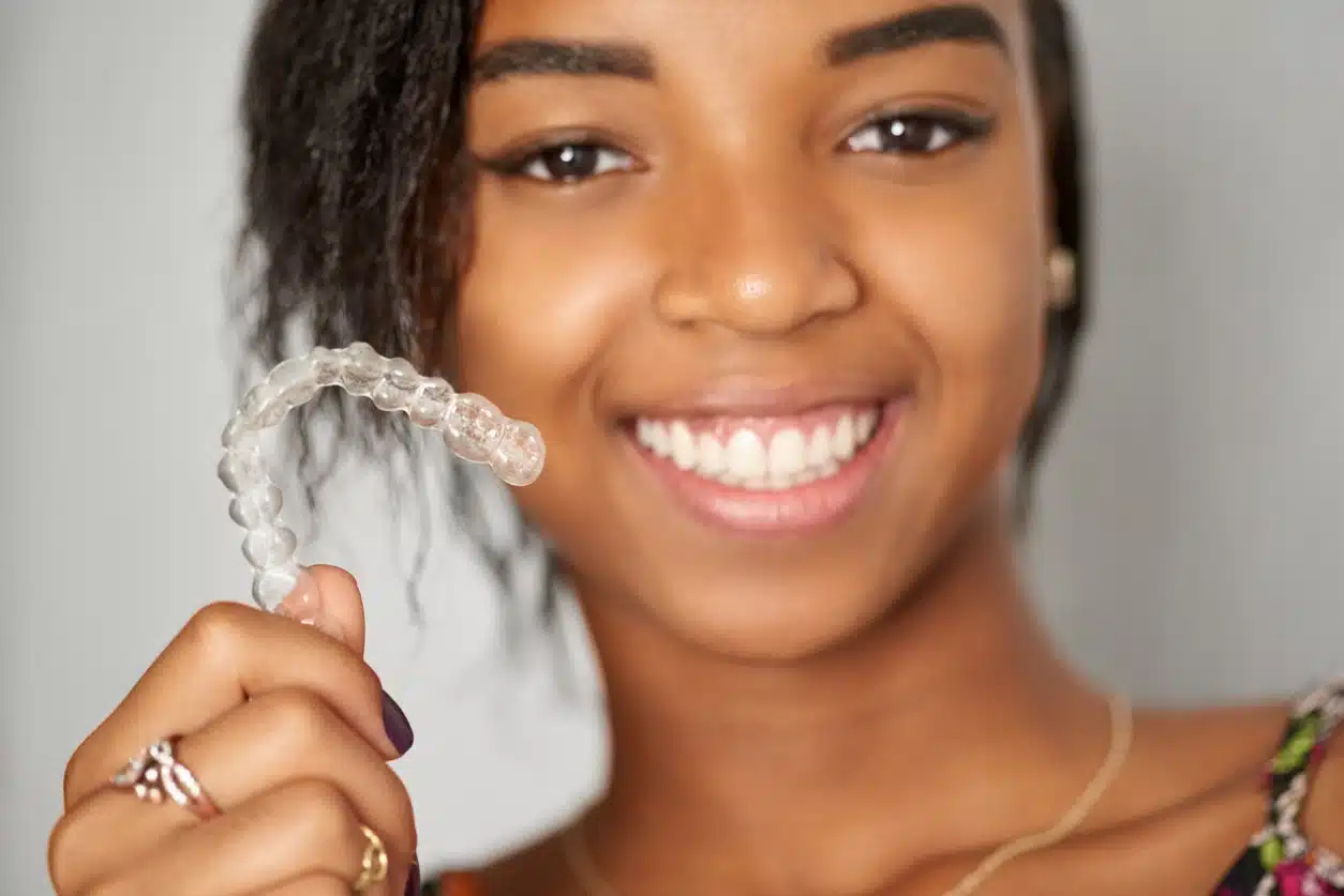a teenage girl holding invisalign clear aligners up in front of her