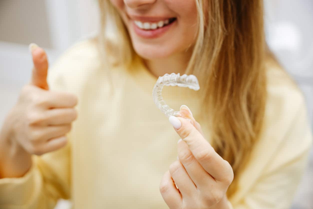 a woman throwing up a thumbs up and holding invisalign on the other hand