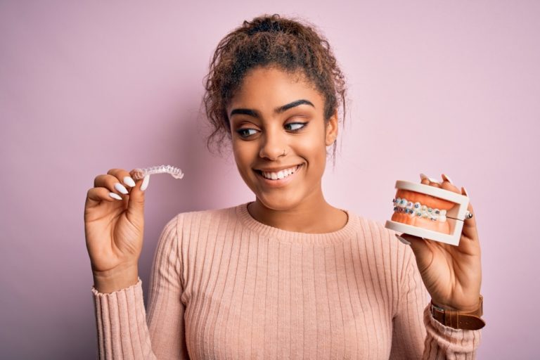 a woman with clear aligners and a braces typodont on each hand
