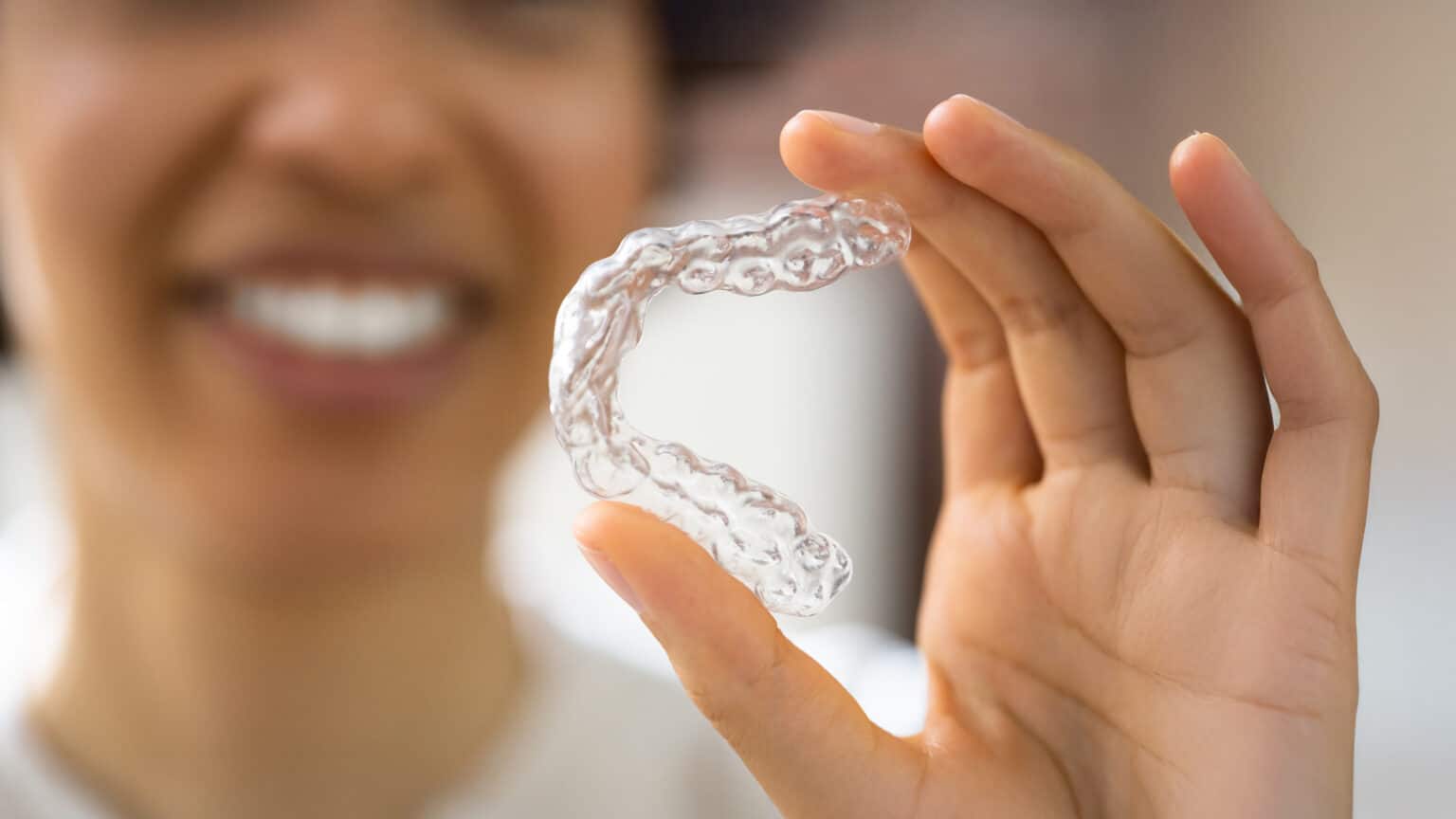 Close-up of an invisible aligner being held by a young woman