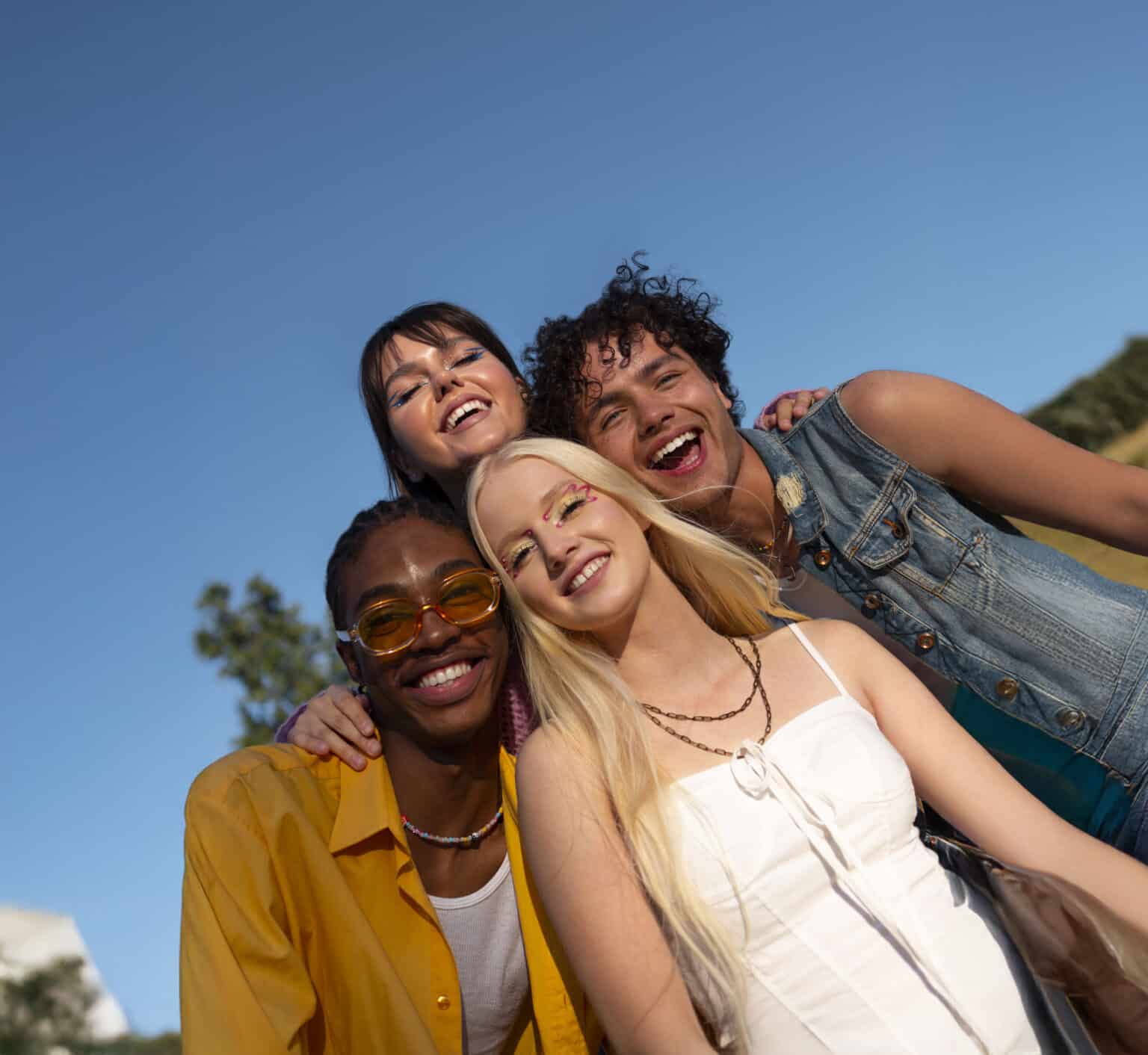 Group of 4 attractive young adults posing for a picture on a cloudless summer day
