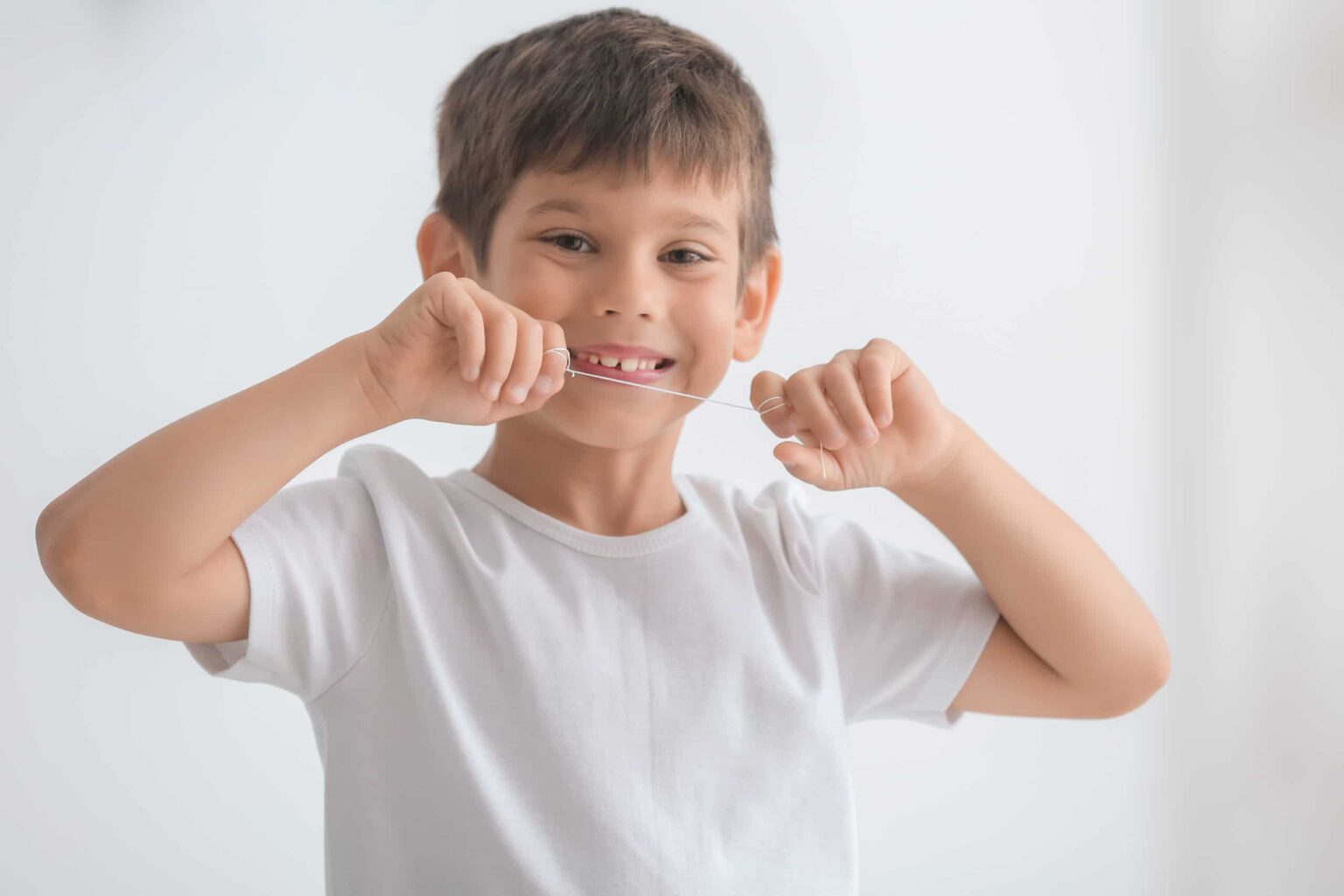 Young boy smiling and holding dental floss wound between his index fingers