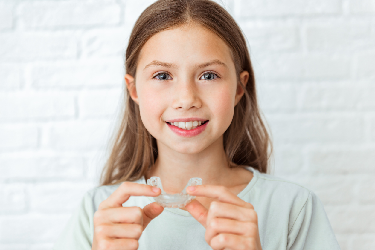 teen holding her aligner in front of her in an orthodontics office