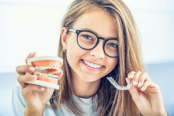 Dental invisible braces or silicone trainer in the hands of a young smiling girl. Orthodontic concept - Invisalign.