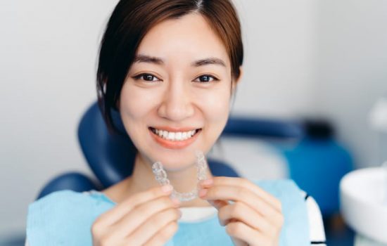 a female patient sitting on the dental chair and holder invisalign clear aligners up to her mouth